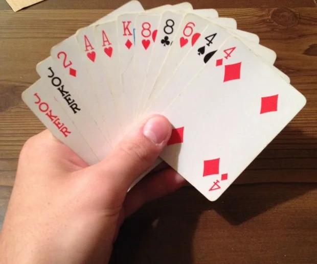 A hand holding playing cards, mostly red suits, fanned out.