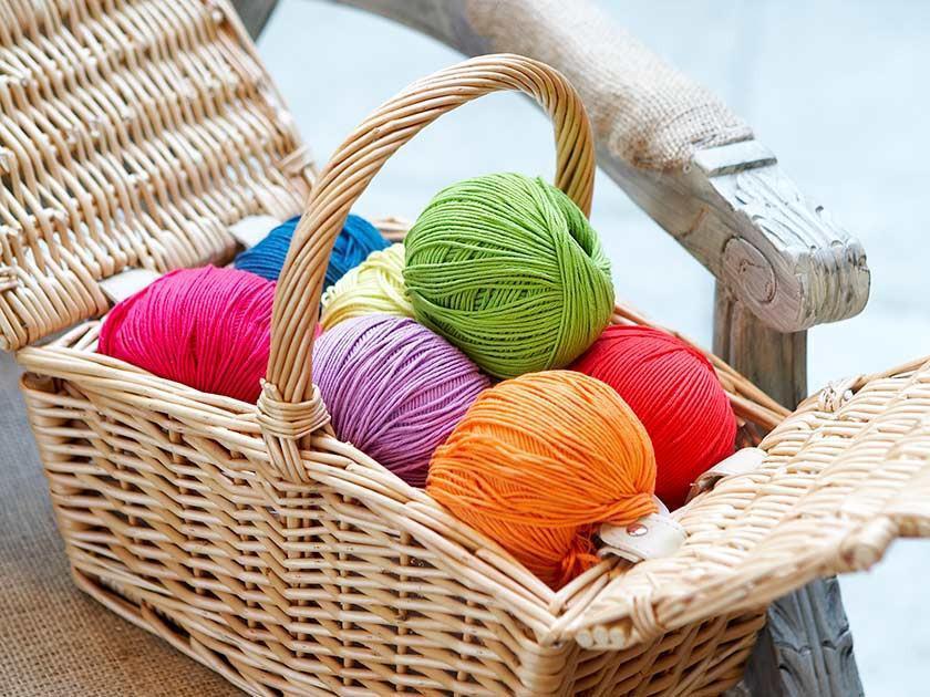 Colorful yarn balls in a wicker basket on a chair.