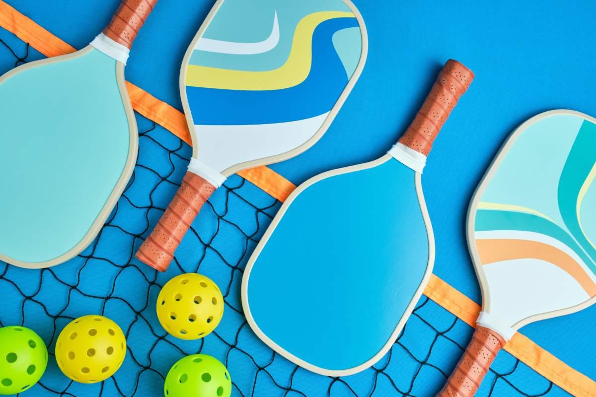 Four colorful pickleball paddles on a blue surface with yellow balls and net.
