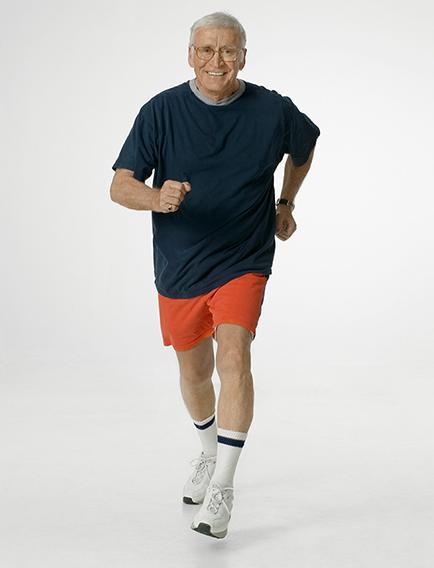 Elderly man jogging in red shorts and navy shirt, smiling.